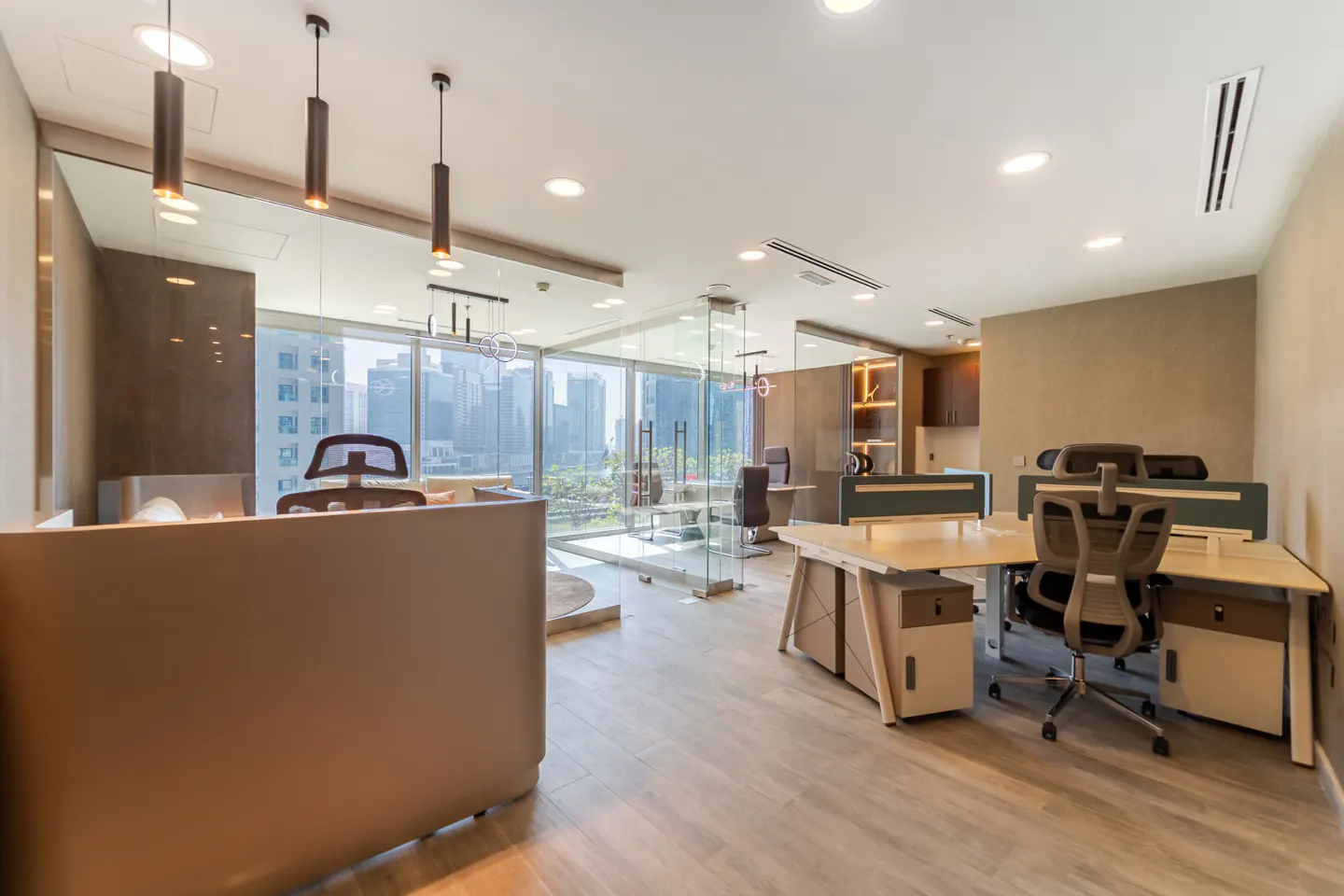 Bright, modern office space with desks, chairs, and glass-walled rooms. Cityscape visible through large windows. Neutral color palette.