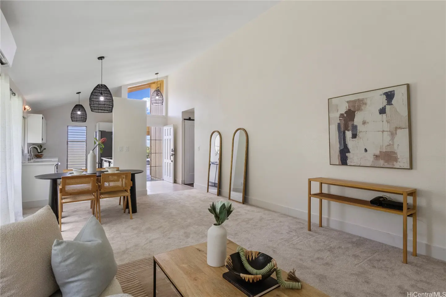 Bright, open-concept living space with neutral tones. Features a dining area, two mirrors, and a wooden console table. Artwork hangs on the wall.