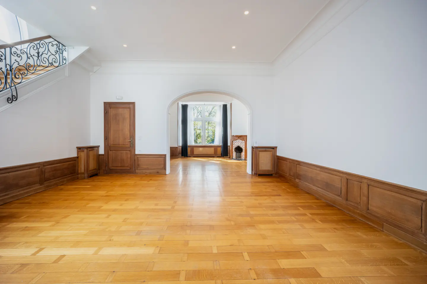 Empty room with wood floors, white walls, and wood trim. A staircase is visible on the left.