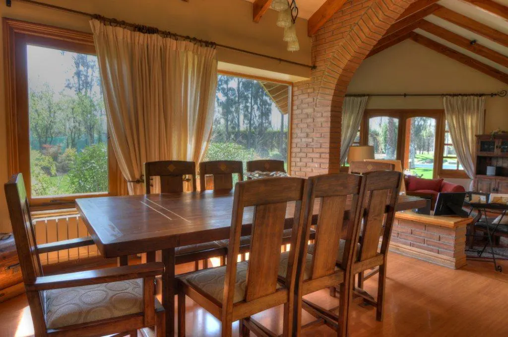 A dining room with a wooden table and chairs, brick archway, and large windows overlooking a green landscape.