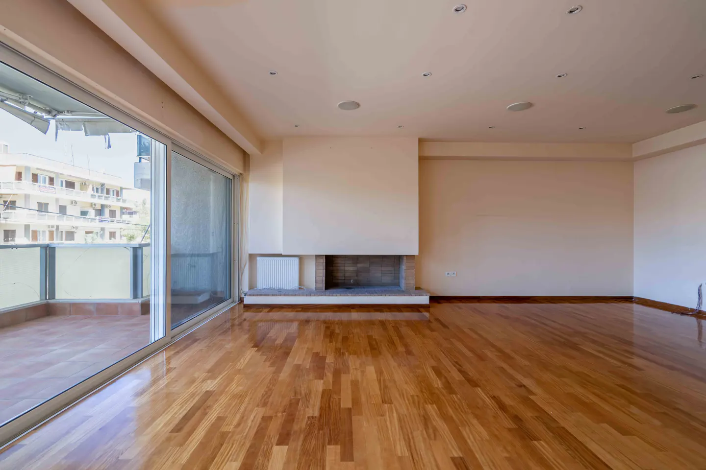 Empty living room with hardwood floors, a fireplace, and sliding glass doors to a balcony. The walls are light beige.