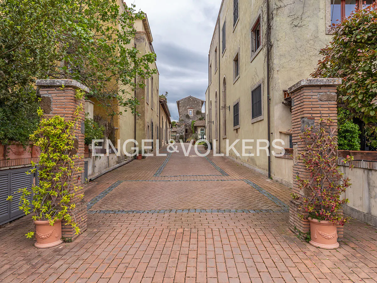 Cobblestone street view between two buildings with brick pillars and potted plants on either side.