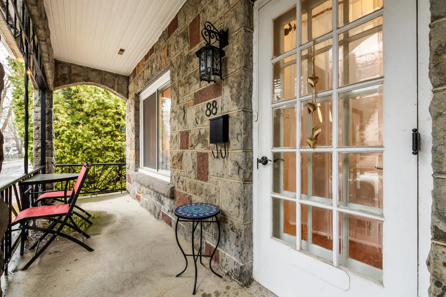 Stone house exterior with a white door, black mailbox, and a porch with red chairs and a table.