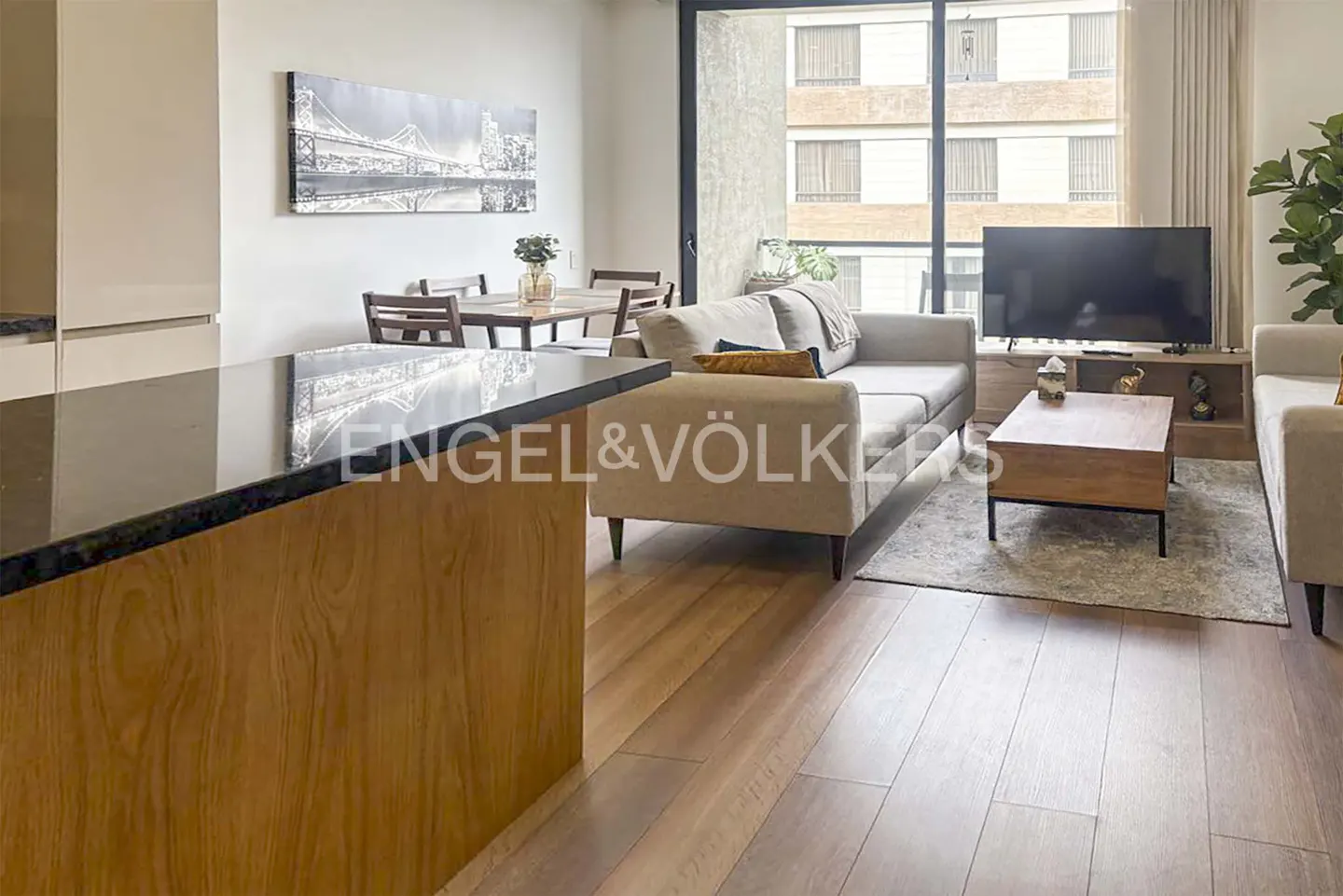 A modern living room with wood floors, a beige sofa, a wood coffee table, and a large window with a view of a building.