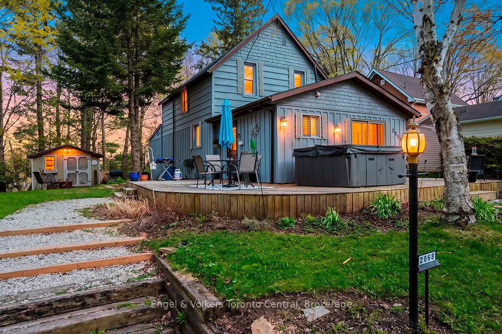 Exterior view of a blue two-story house with a deck, hot tub, and shed at dusk. A stone path leads to the house.