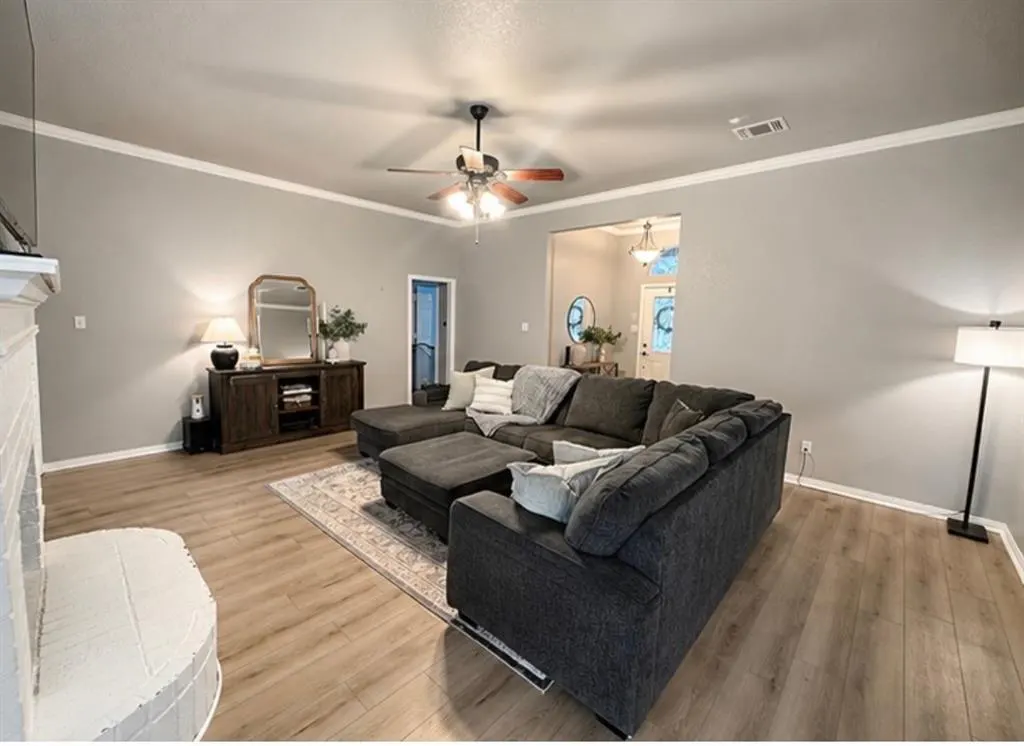 Living room with gray walls, wood floors, and a large gray sectional sofa. A ceiling fan and a wood cabinet with a mirror are also visible.