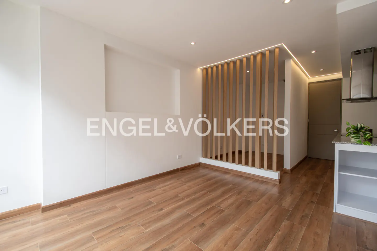 Bright, modern apartment interior with wood floors, white walls, and a slatted wood partition. Engel & Völkers logo is superimposed.