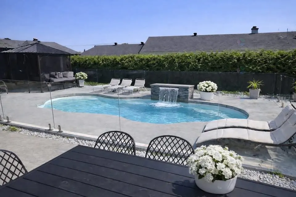 Backyard with a blue pool, waterfall feature, lounge chairs, black table and chairs, and a gazebo.