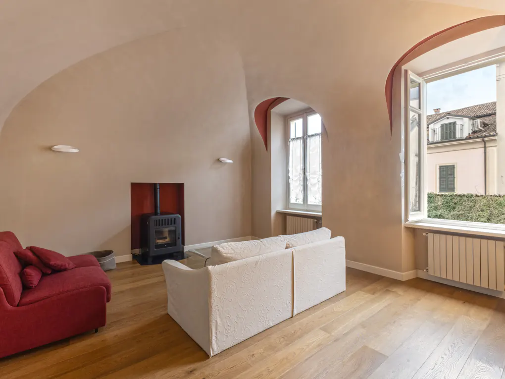 Living room with arched ceiling, wood floors, and red accents. A white sofa faces an open window with a view of a building.