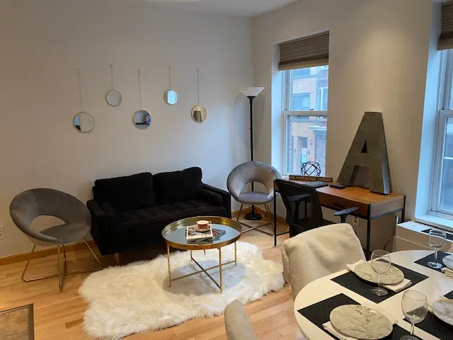 Living room with black sofa, round mirrors, gold table, desk with large "A", and dining table set for a meal.