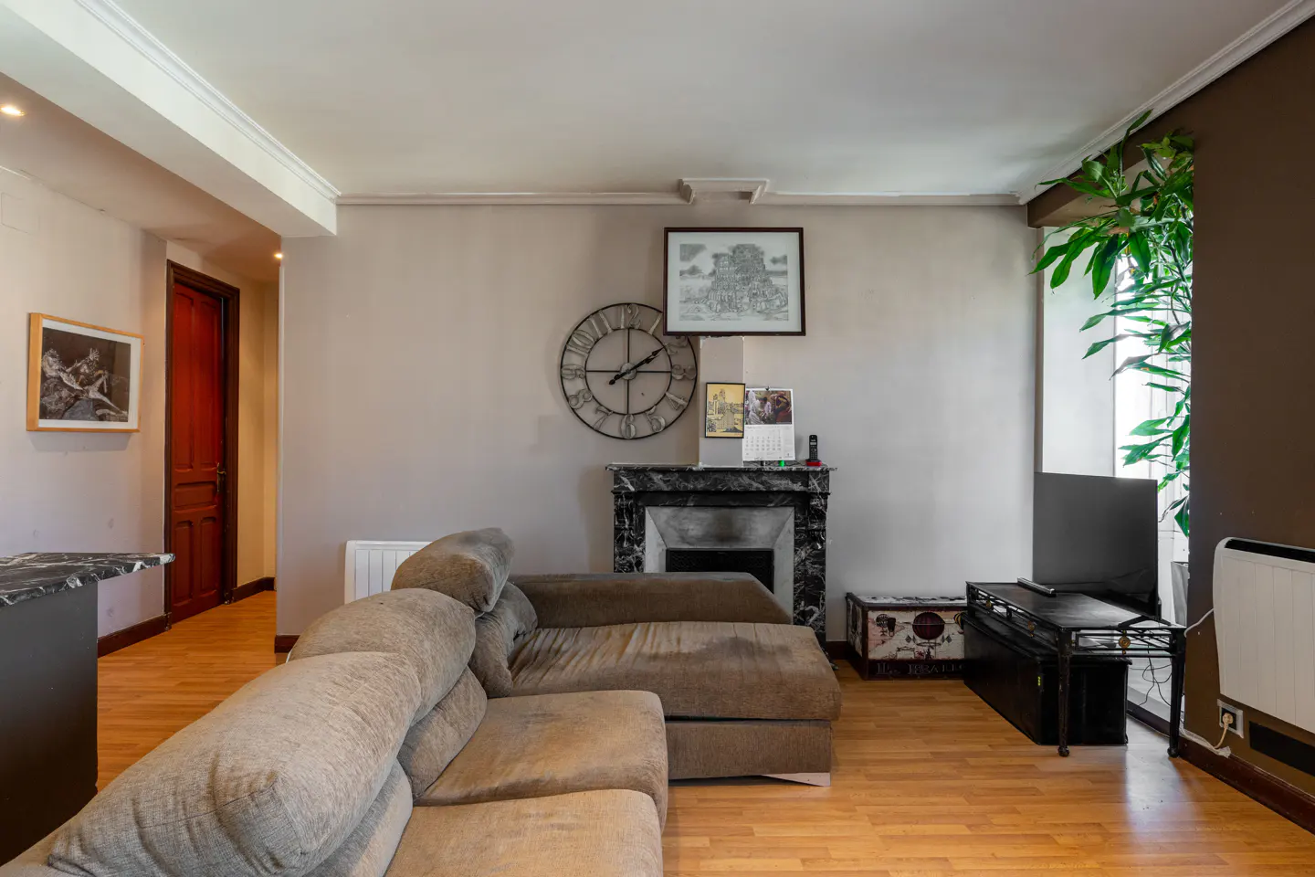Living room with a brown sectional sofa, fireplace, TV, and wood floors. A large clock hangs on the wall.