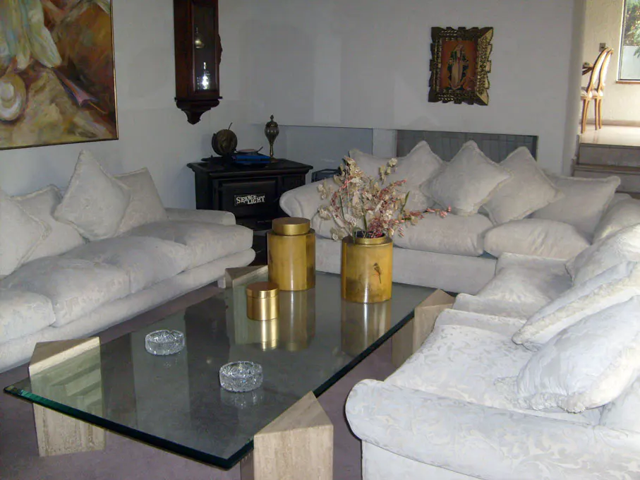 Living room with white sofas, glass table, and gold decorative jars. A dark wood clock hangs on the wall.