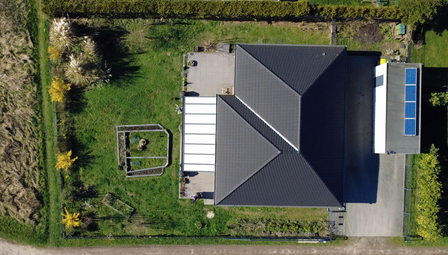 Aerial view of a house with a dark gray roof, solar panels, a white awning, and a green lawn.