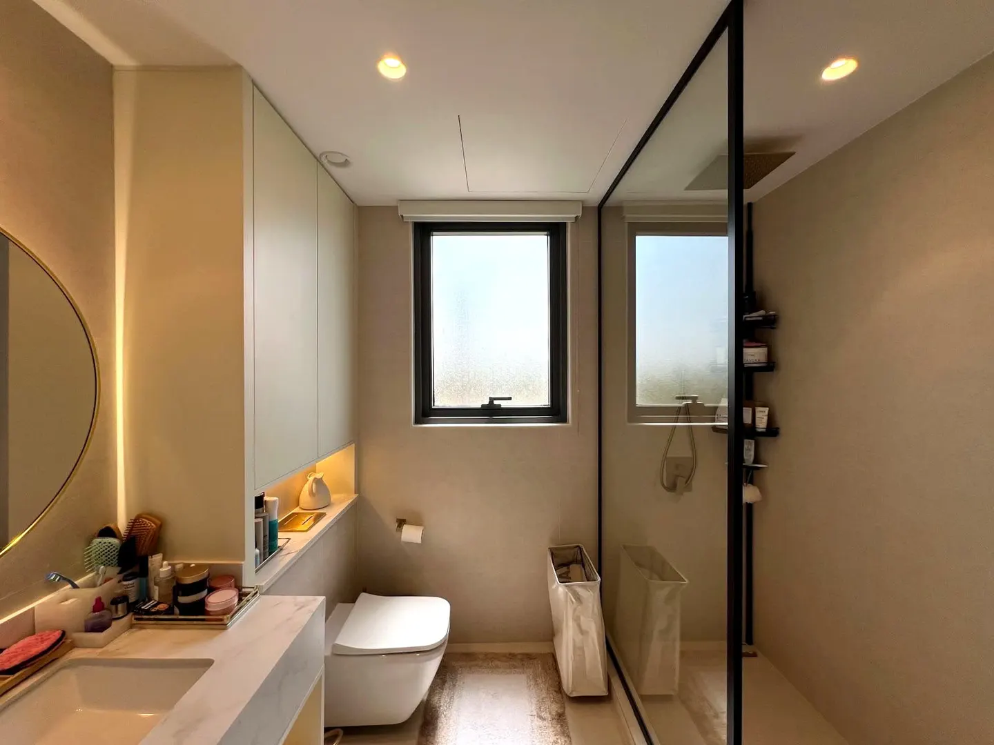 Modern bathroom with a marble vanity, wall-mounted toilet, and a glass-enclosed walk-in shower with black trim.