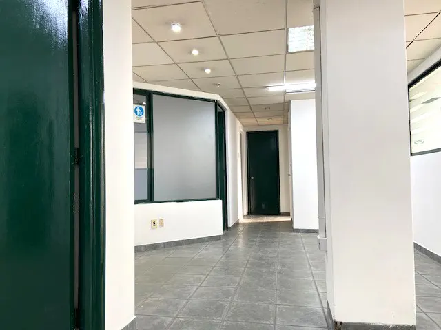 Empty office space with gray tile floor, white walls, and a green door on the left.