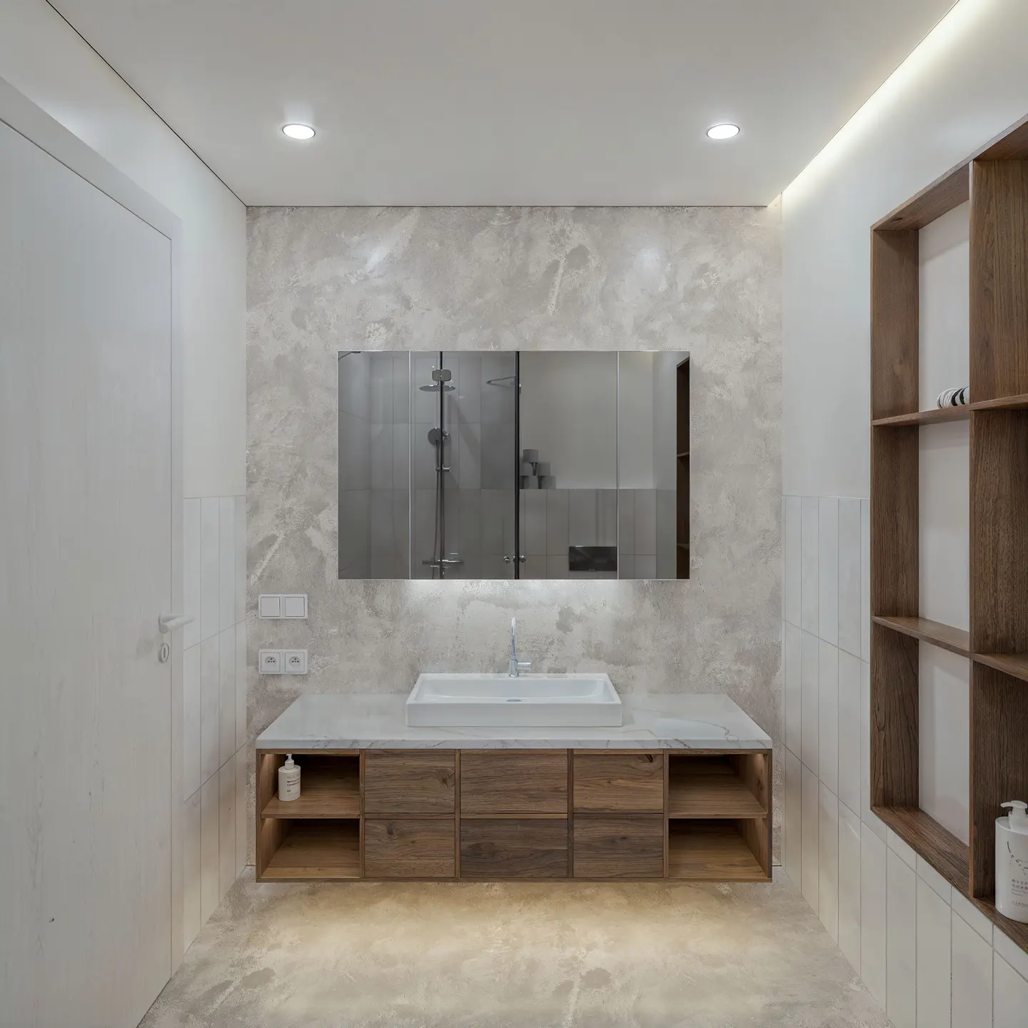 Bright bathroom with marble walls, a wood vanity with a white sink, and a large mirror reflecting a shower. A wood shelving unit is on the right.