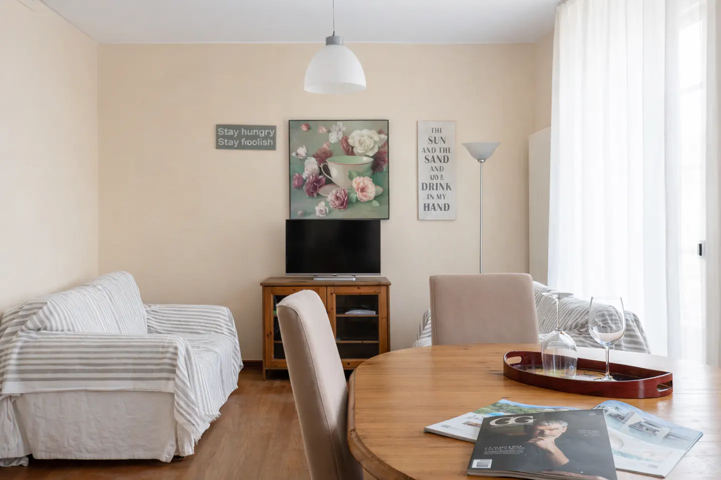 Living room with a striped sofa, wooden table with magazines, and a TV on a wooden cabinet. Artwork adorns the wall.