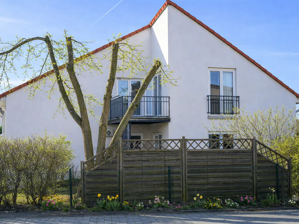 A two-story white house with a red roof, a balcony, and a wooden fence in front.