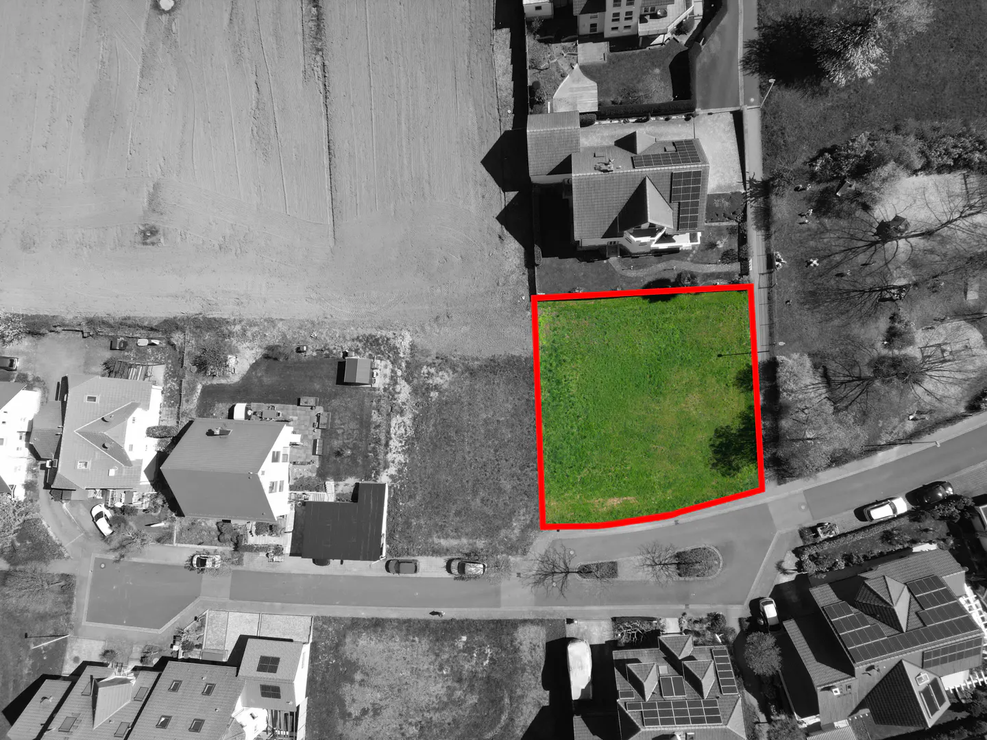 Aerial view of a green lot outlined in red, surrounded by grayscale houses and streets.