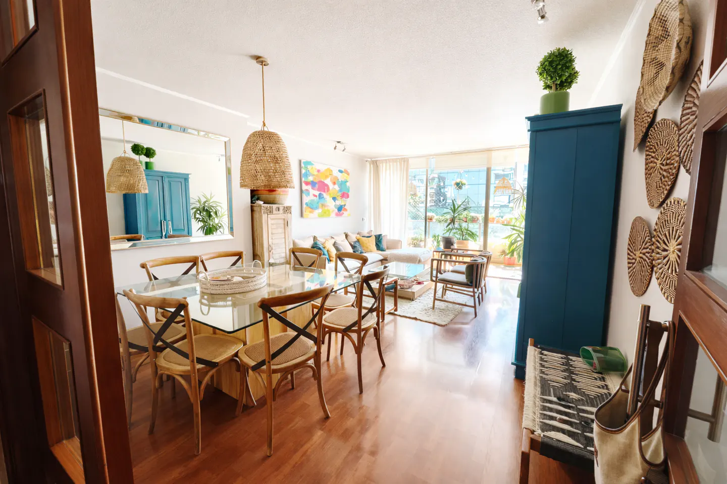 Bright, open-concept living space with dining table, glass top, wooden chairs, blue cabinet, and balcony with plants.