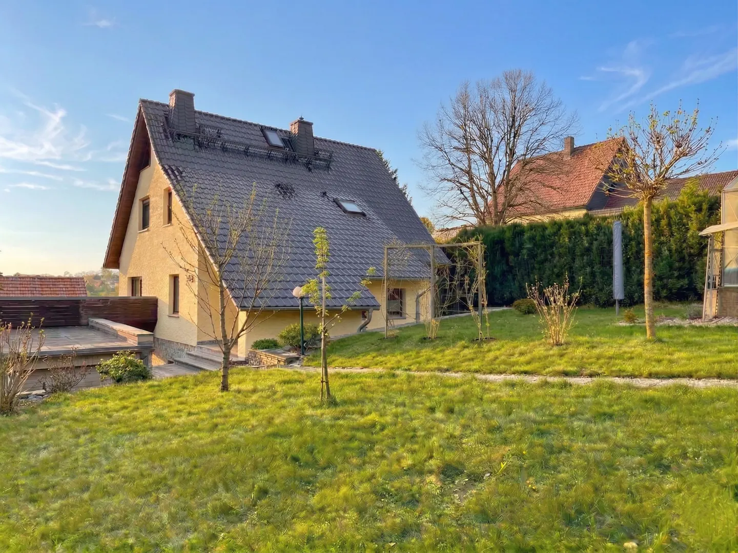 A yellow two-story house with a gray roof sits on a green lawn under a blue sky.