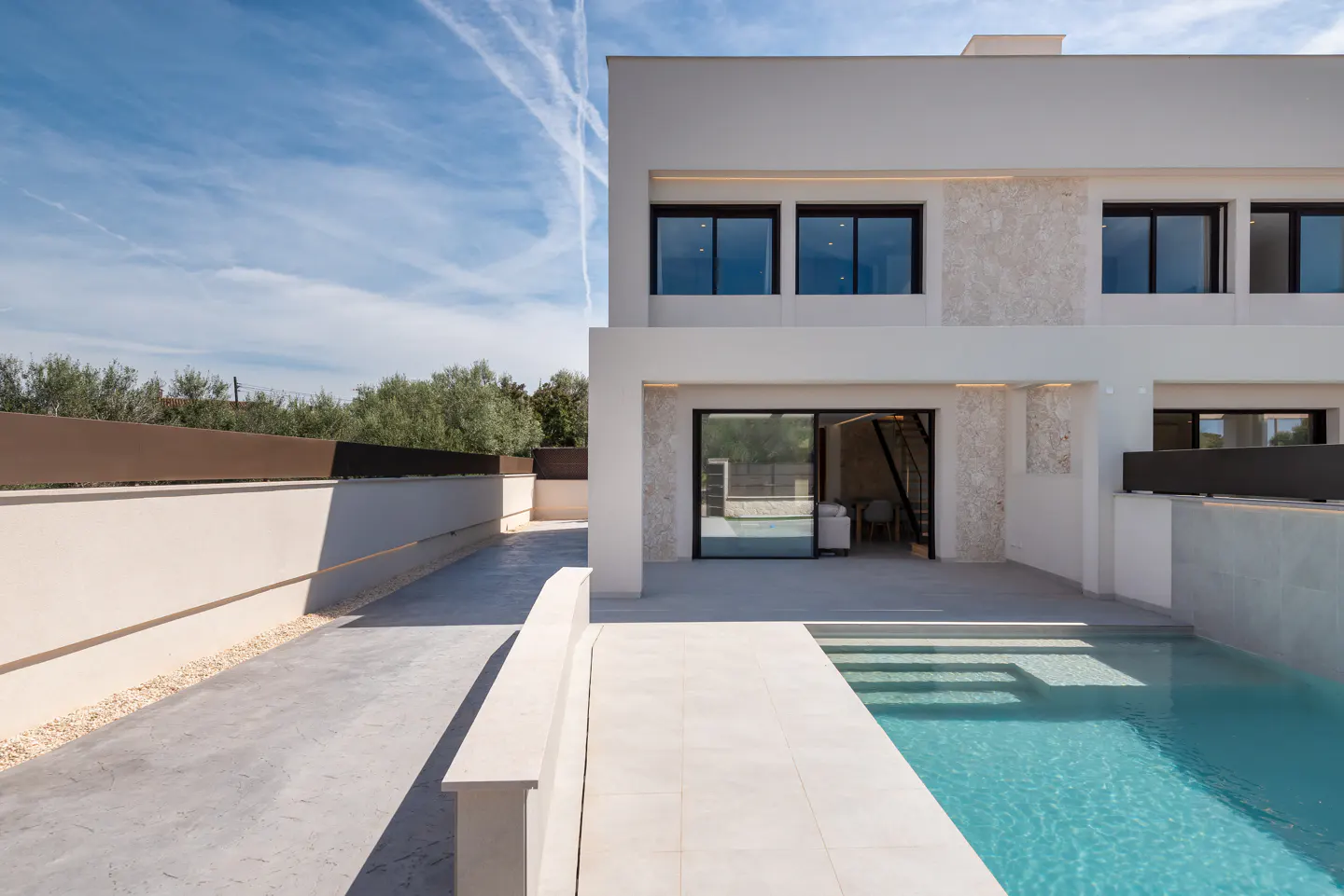 Modern white house with a pool. The house has black framed windows and a sliding glass door. Blue sky with clouds in the background.