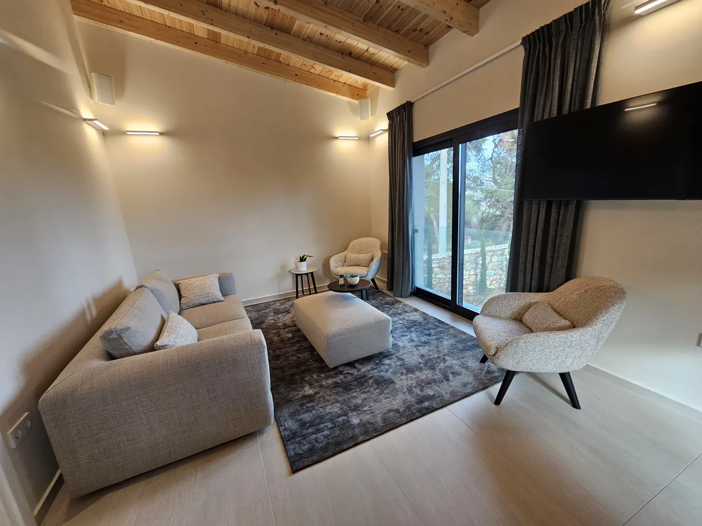 Living room with a gray sofa, two armchairs, and a gray rug. A large window with gray curtains is on the right.