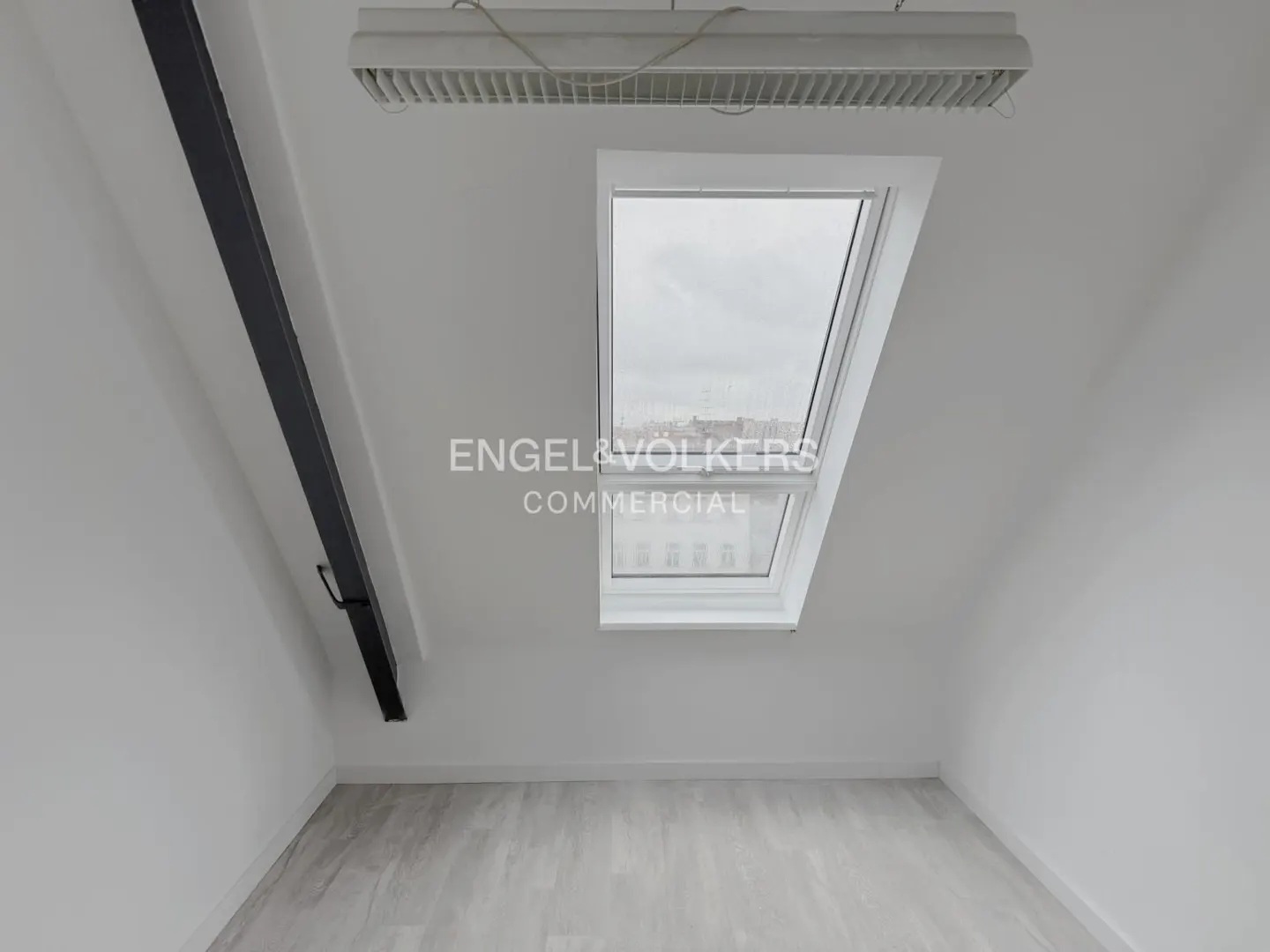Attic room with white walls, light wood floor, black beam, skylight, and ceiling light.
