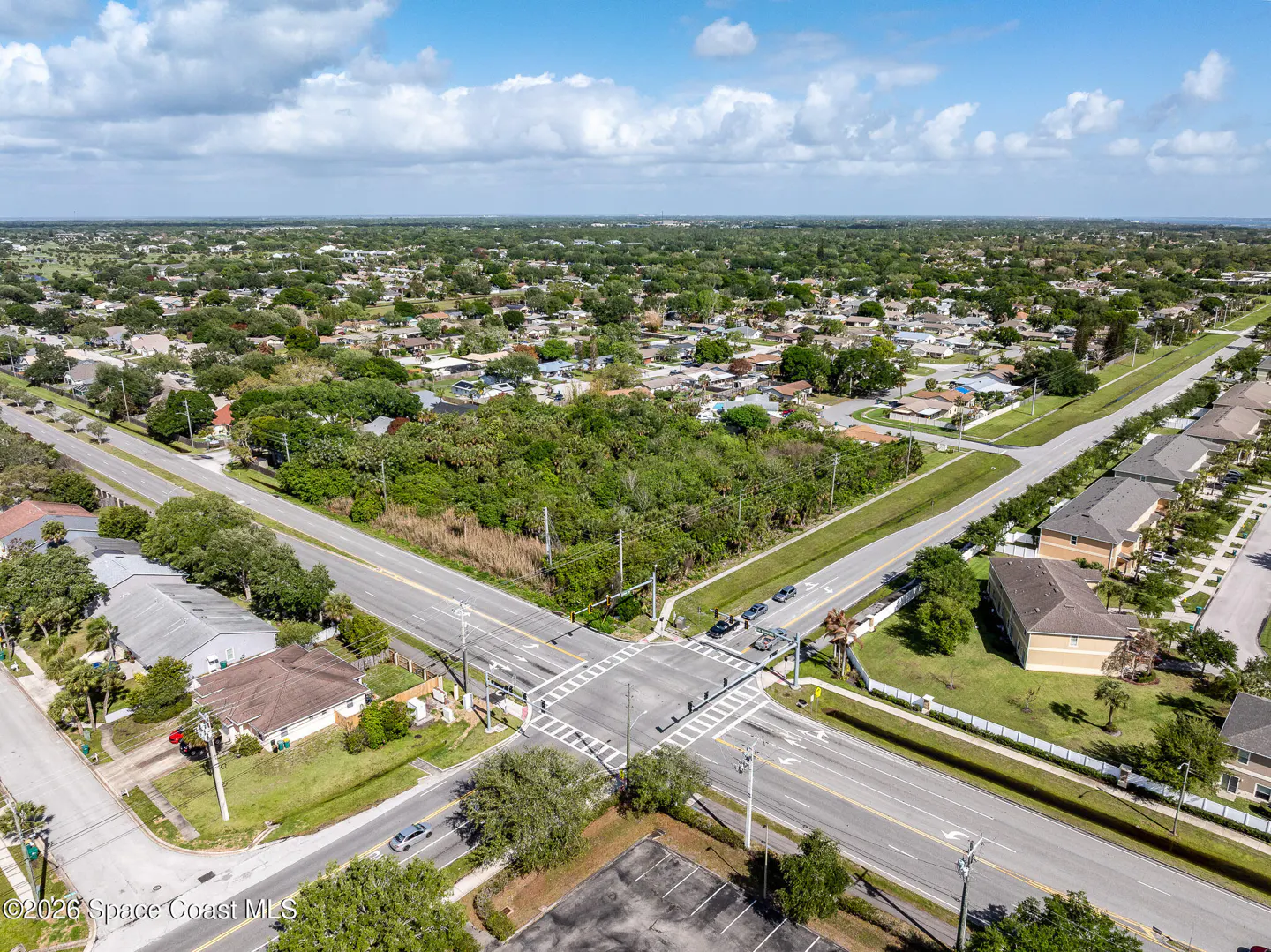 Aerial view of a suburban neighborhood with houses, trees, and a four-way intersection with crosswalks and cars.