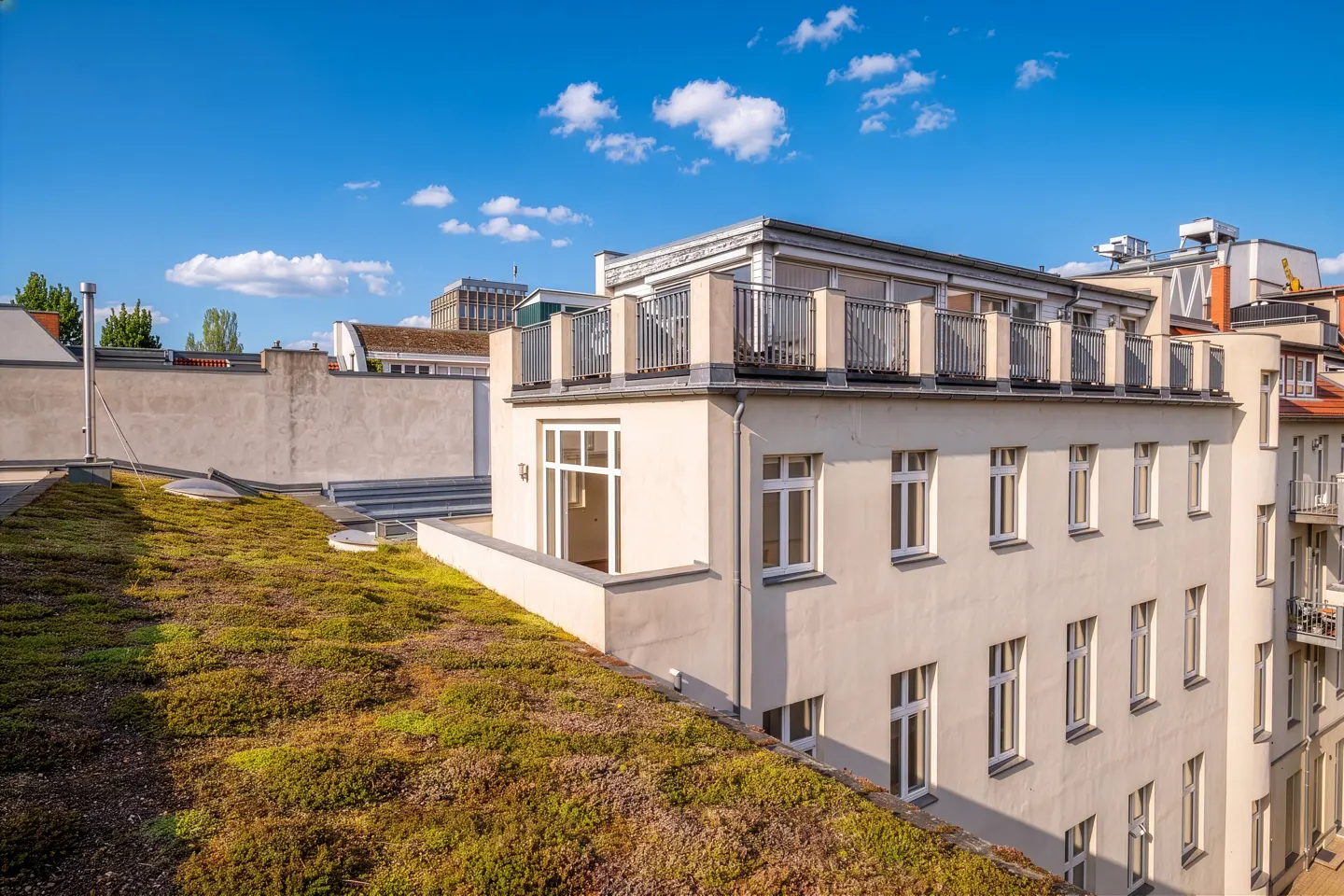 Exterior view of a white building with a green roof under a blue sky with white clouds.