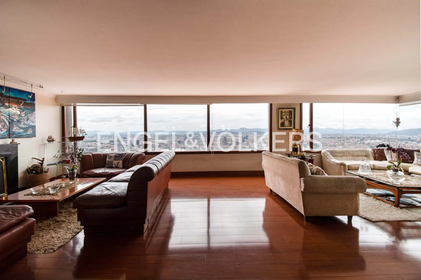 A spacious living room with hardwood floors, leather sofas, and a city view through large windows.