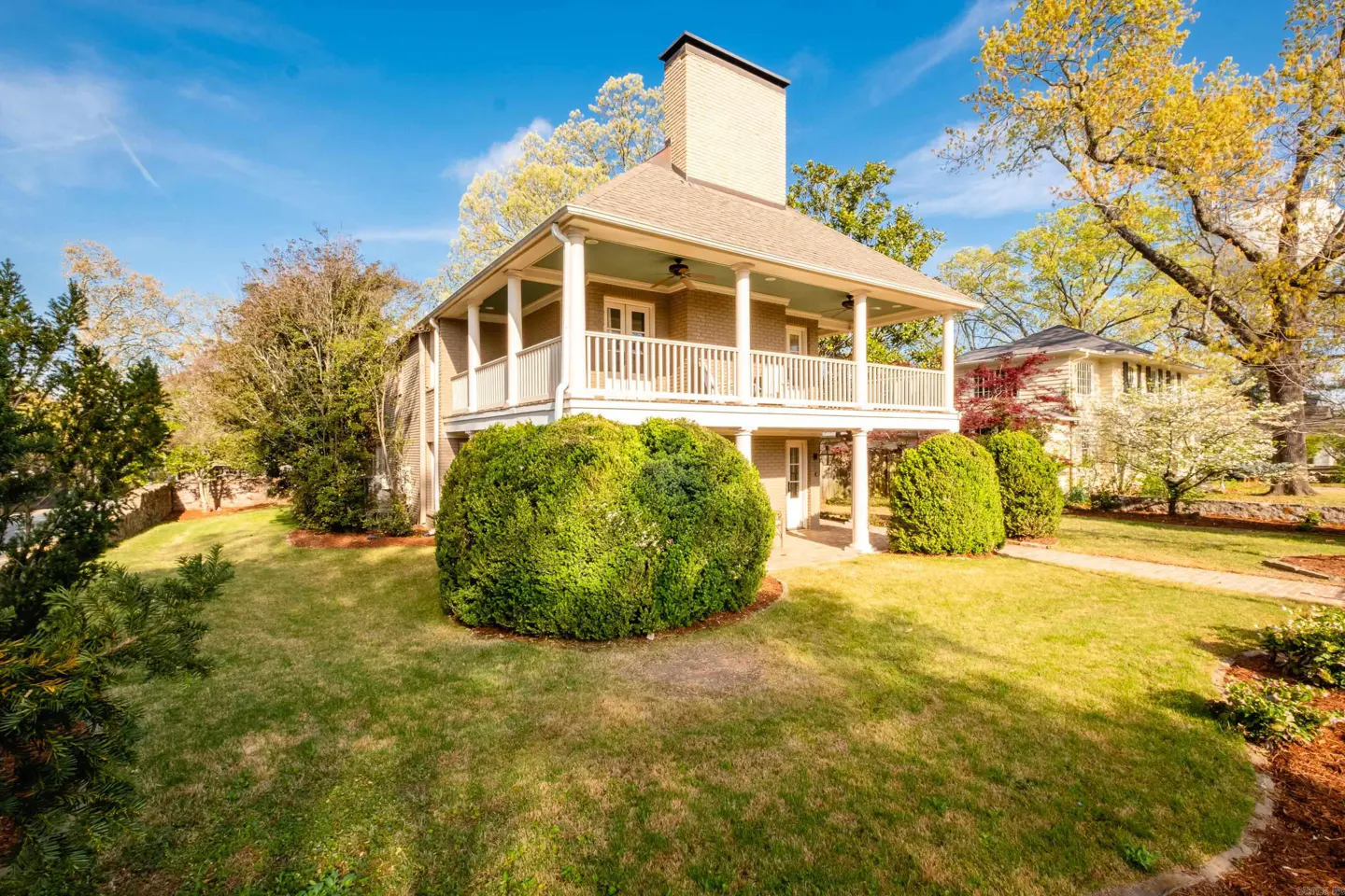 Two-story house with a large chimney, white porch, and green lawn under a blue sky.