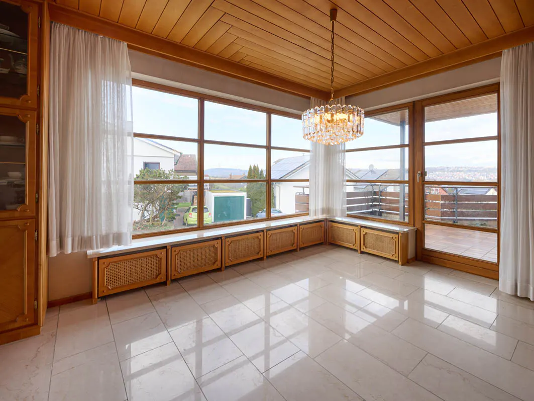 Bright room with wood ceiling, large windows, and tile floor. A crystal chandelier hangs from the ceiling. White curtains frame the windows.