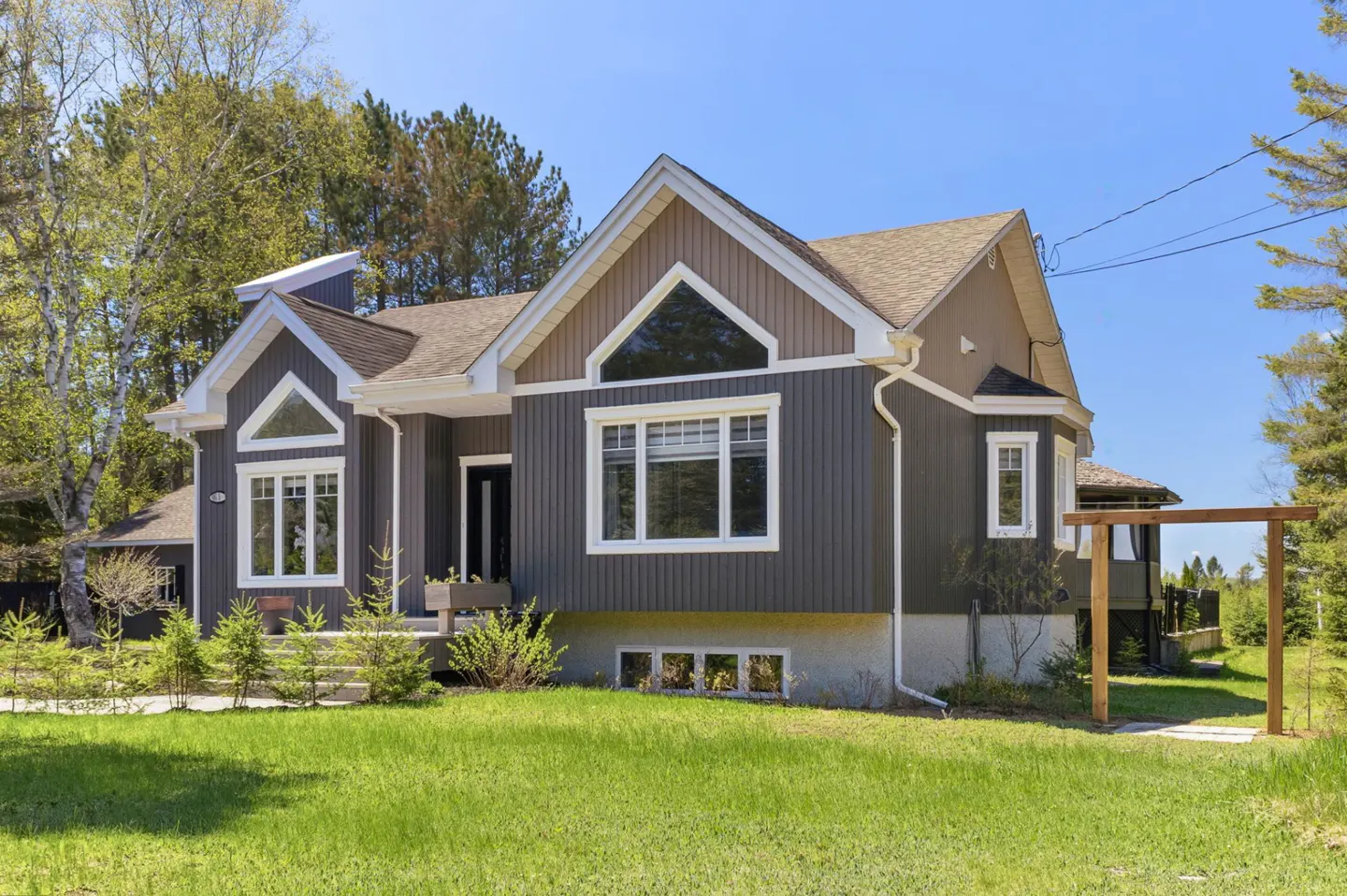 Two-story house with gray siding, brown trim, and a green lawn on a sunny day.
