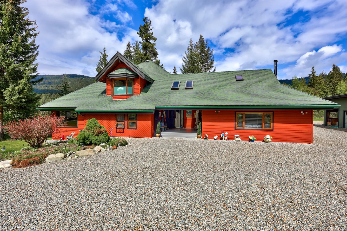 A bright orange house with a green roof sits on a gravel driveway under a cloudy sky.