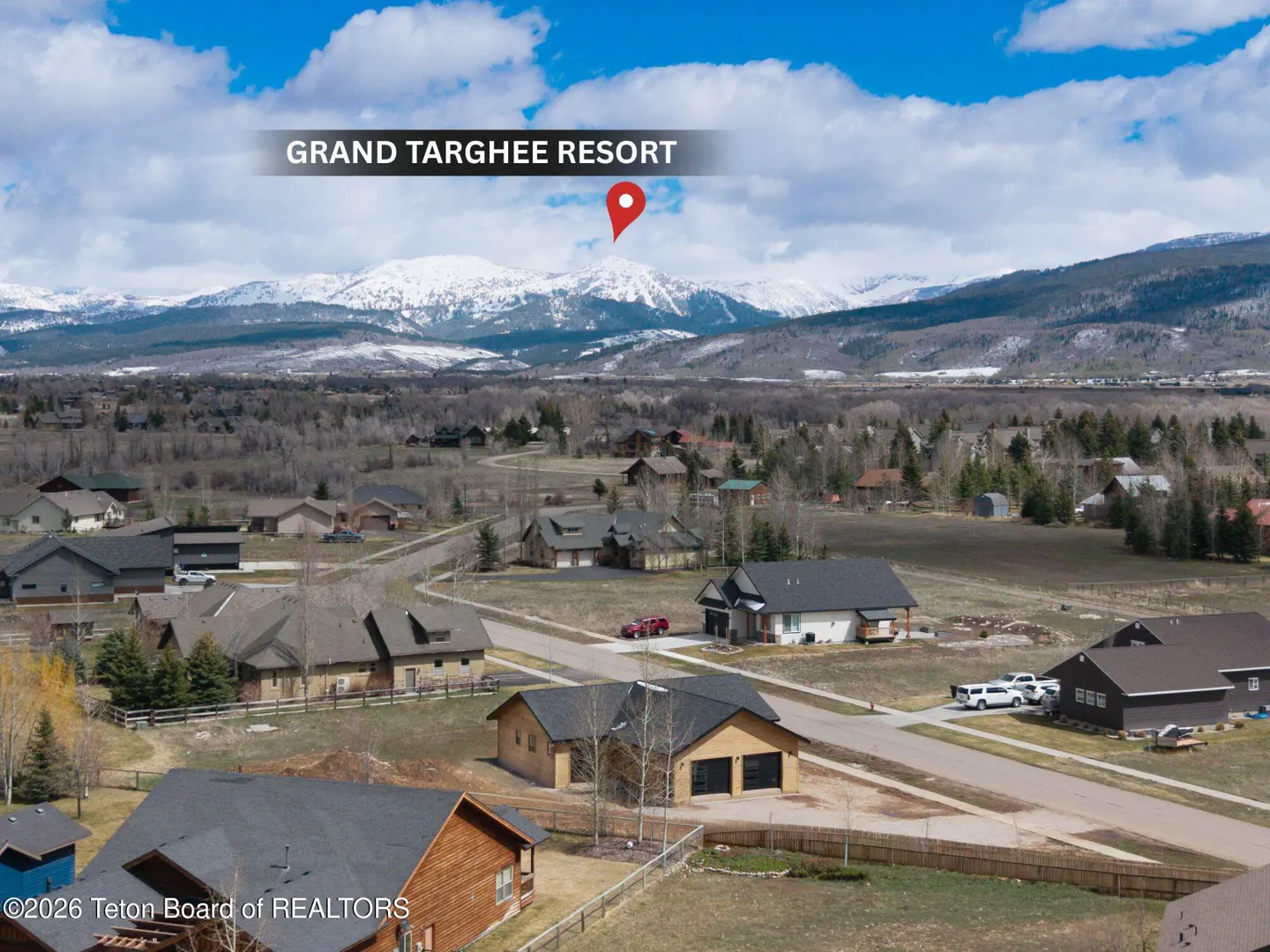 Grand Targhee Resort aerial view. Houses below, snow-capped mountains in the background, blue sky with clouds above.
