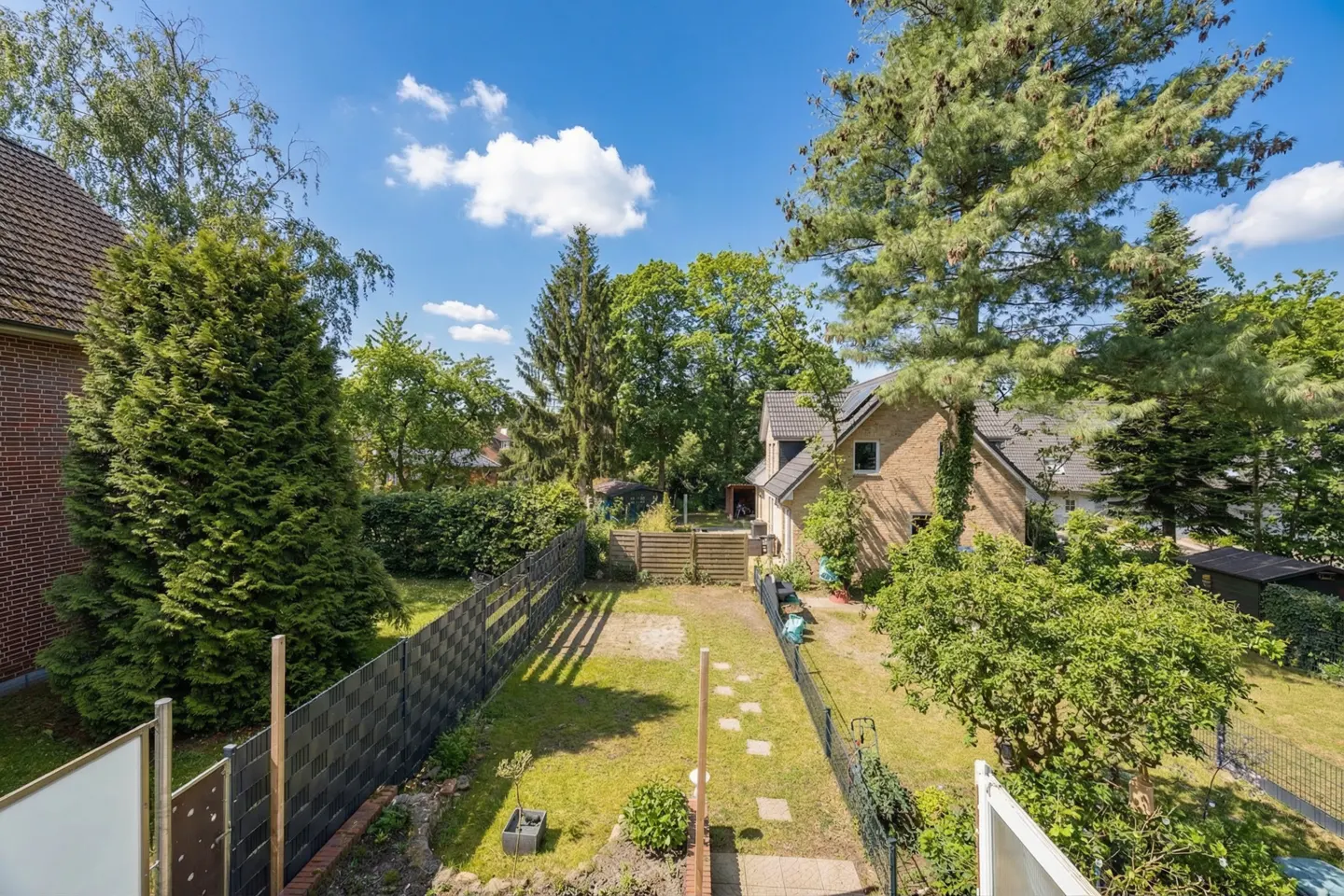 A high angle view of a backyard with a lawn, trees, and a fence on a sunny day.