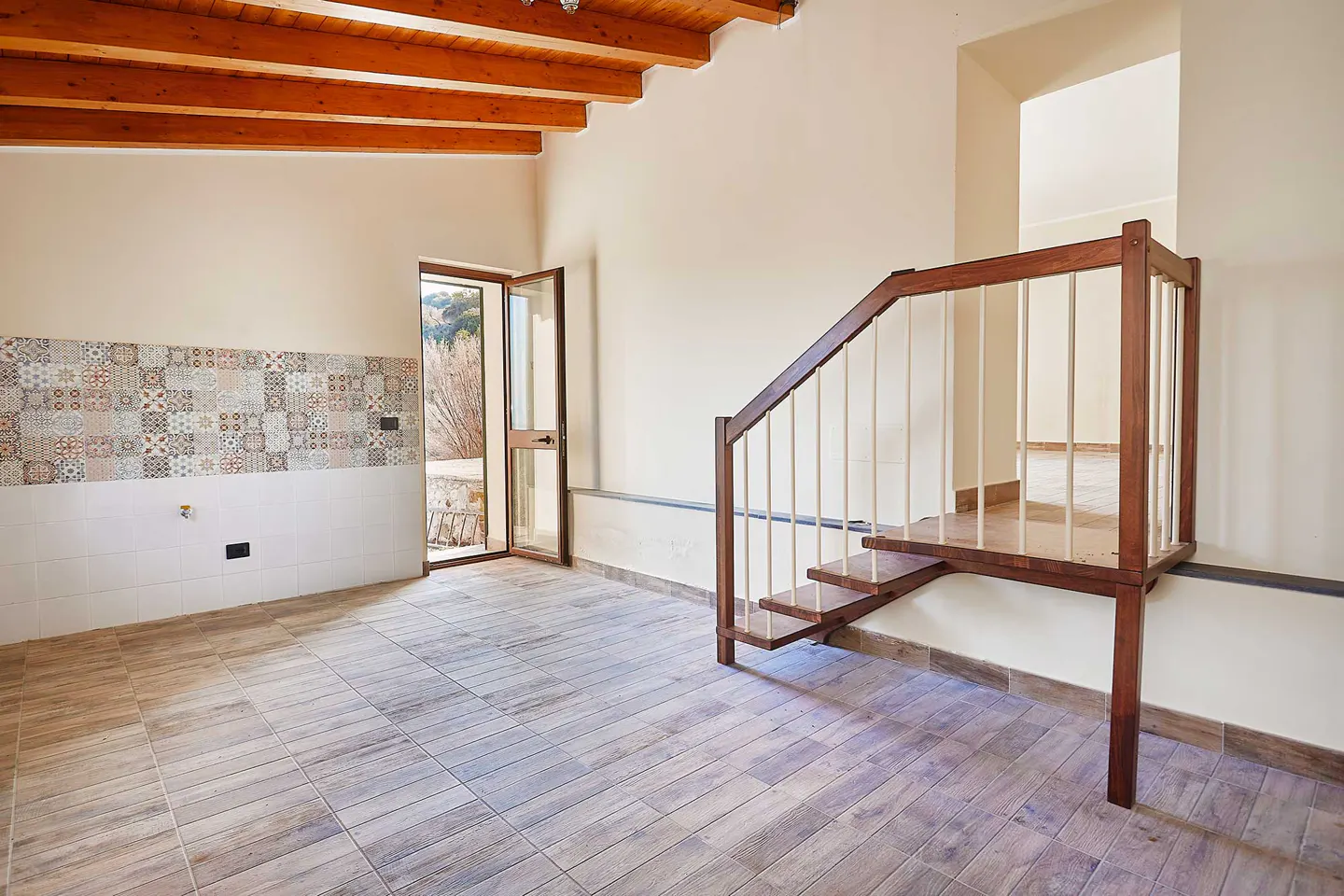 An interior view of a room with wood-look tile flooring, a wooden staircase, and a door to the outside.