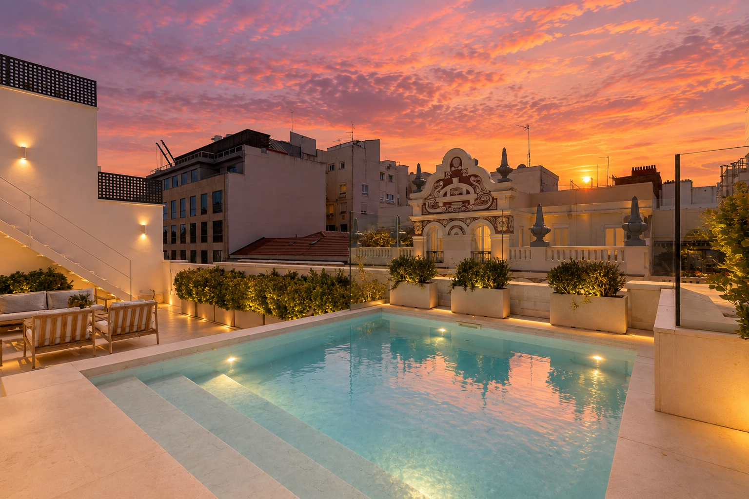 Rooftop terrace with a lit swimming pool, lounge seating, and planters against a vibrant orange and pink sunset city skyline. [AI-generated text]