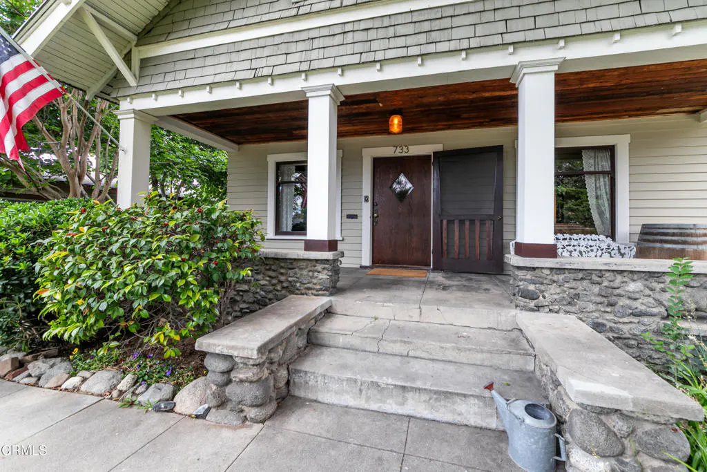 Exterior view of a house with a stone porch, brown door, white pillars, and an American flag.