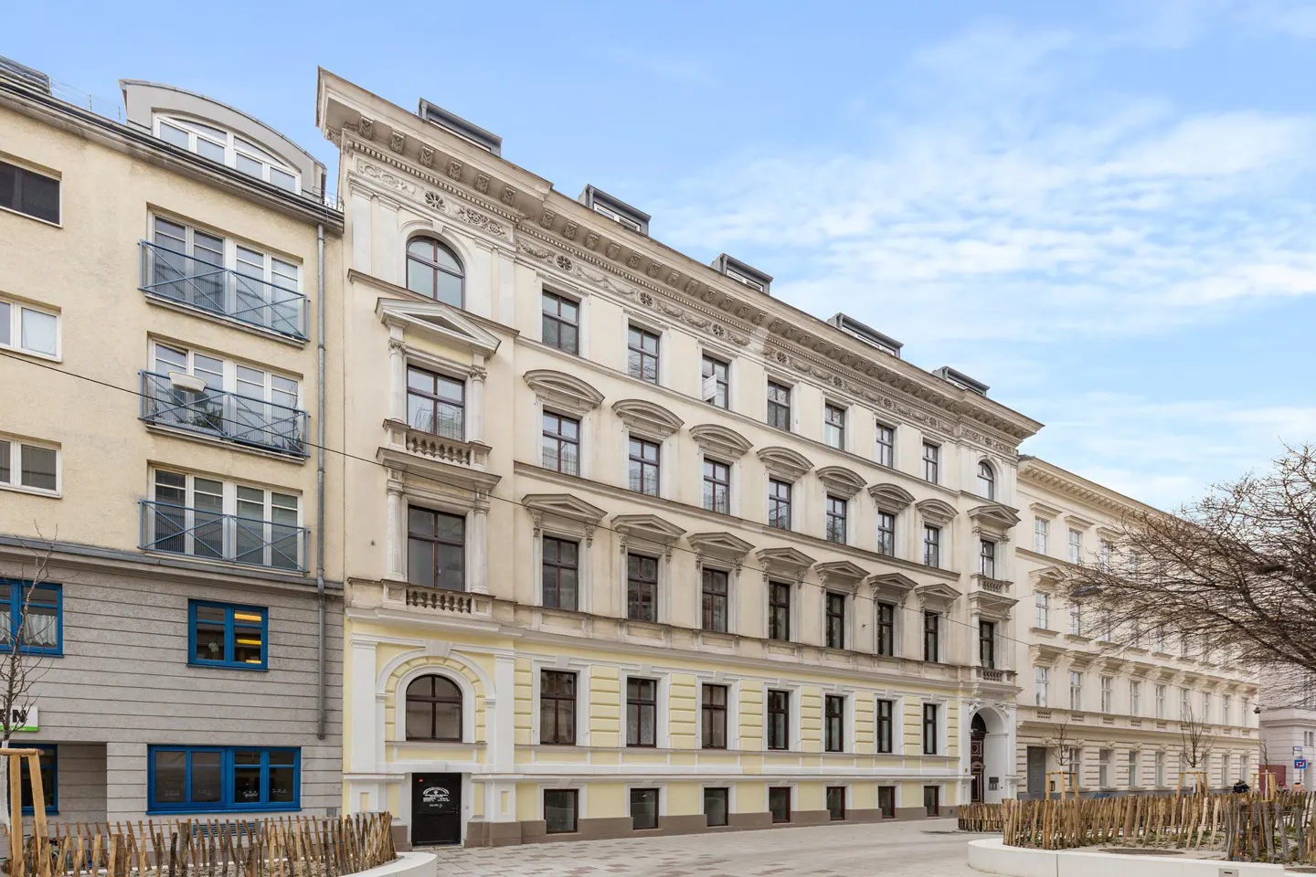 A multi-story, cream-colored historic apartment building with ornate architectural details under a clear blue sky.