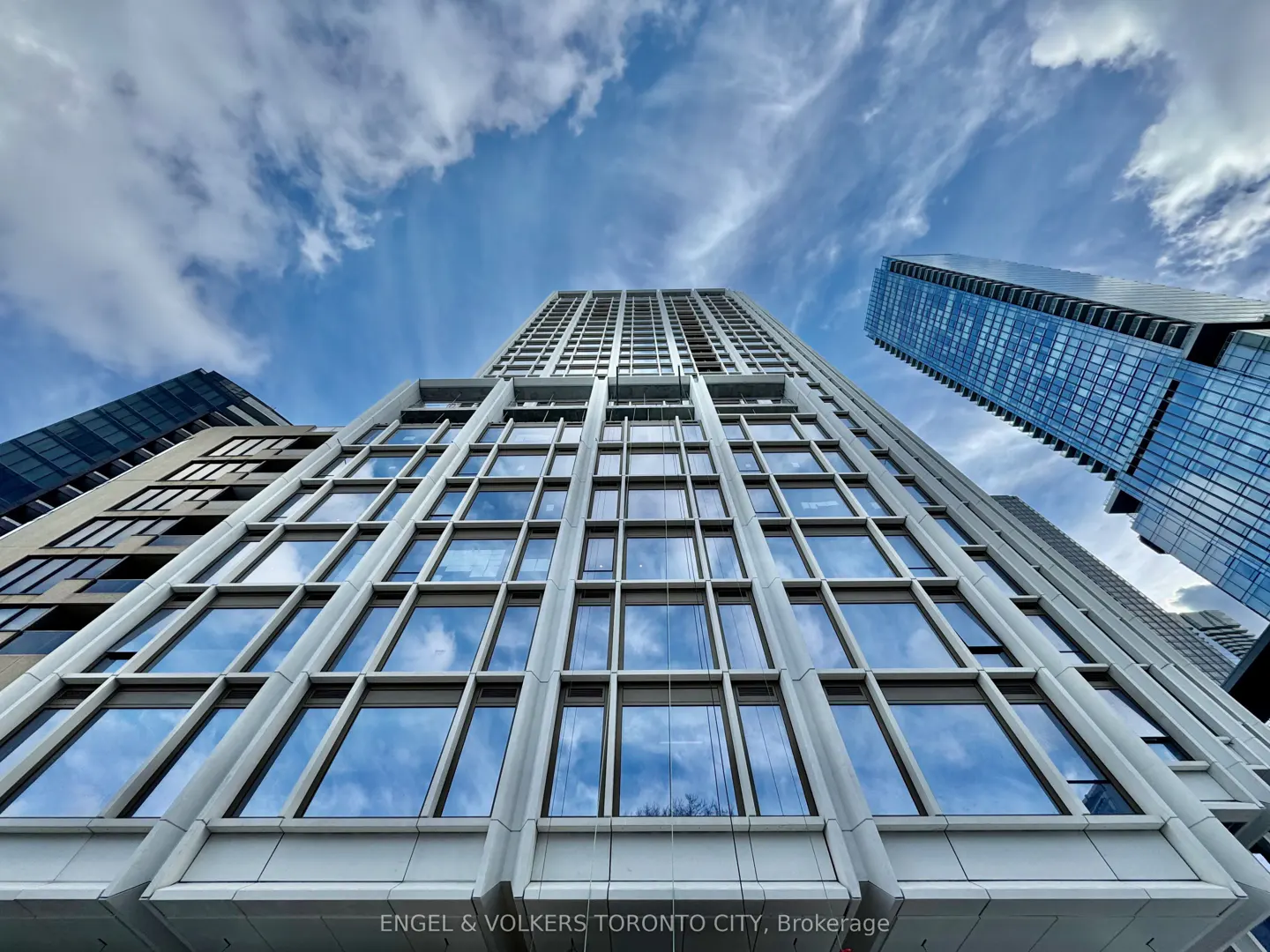 Looking up at a tall, modern building with many windows reflecting the blue sky and clouds.
