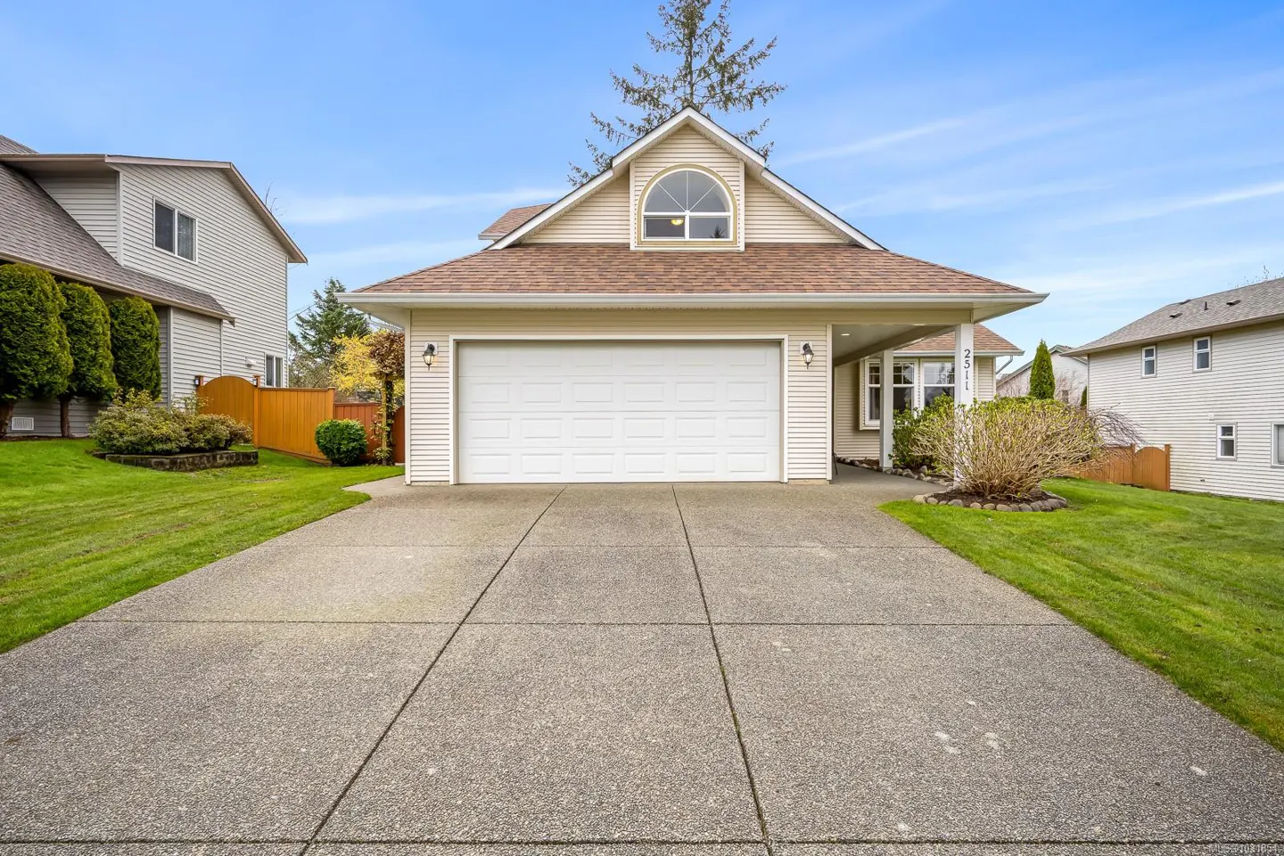 Beige house with a white garage door and brown roof. A concrete driveway leads to the house, with green grass on either side.