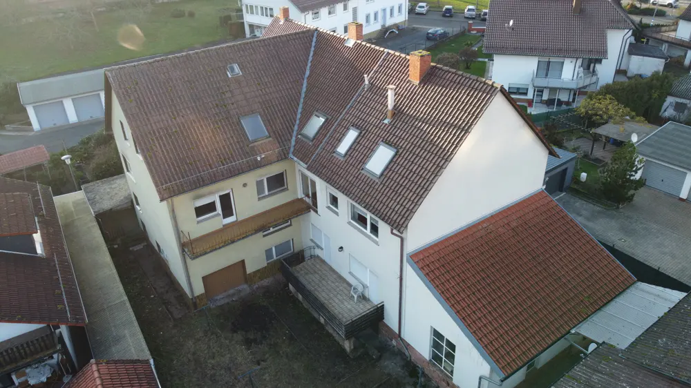 Aerial view of a multi-family home with a red tile roof, light yellow and white siding, and a small backyard.