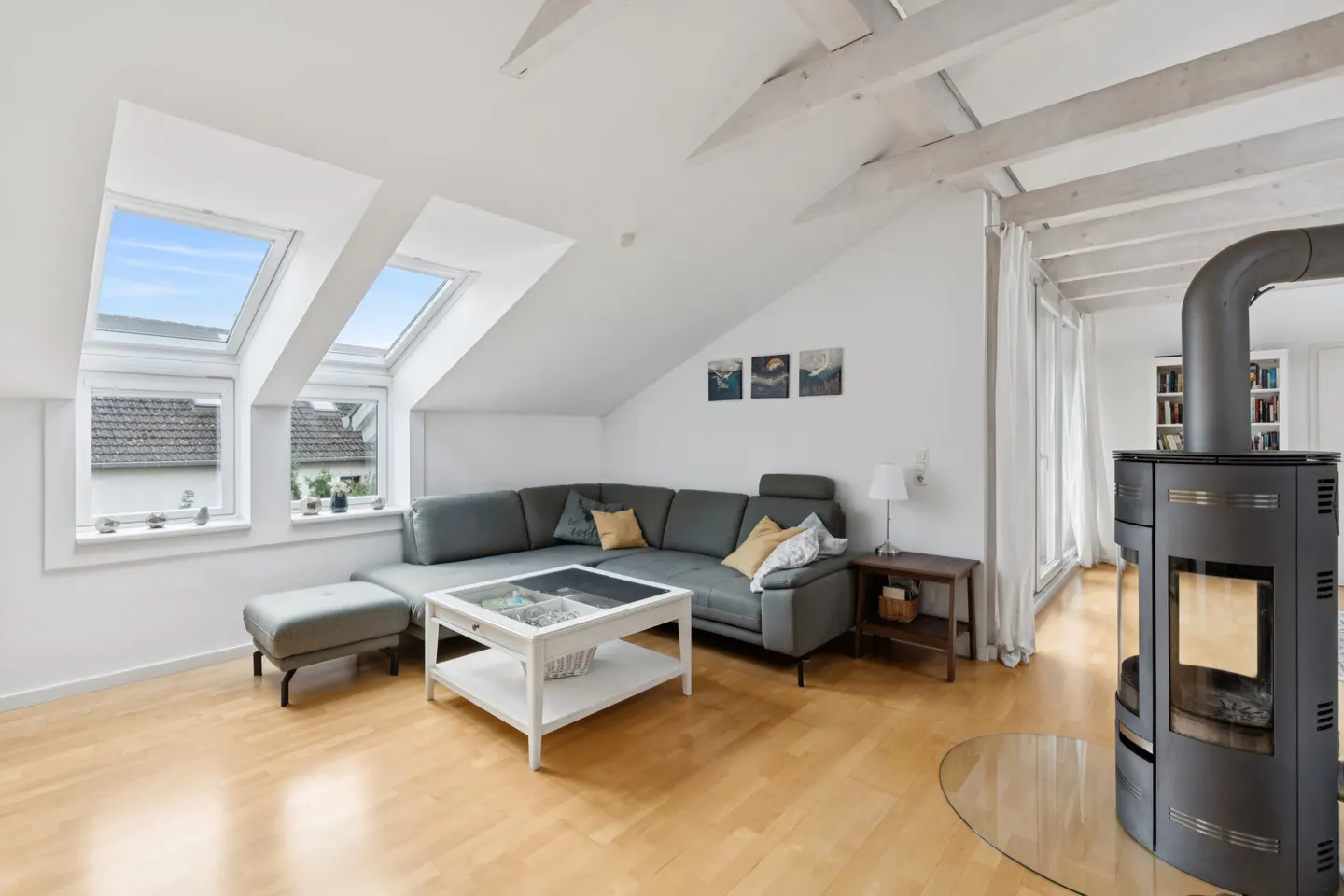 Bright living room with wood floors, gray sectional sofa, white coffee table, and a modern black fireplace. Skylights and windows let in natural light.
