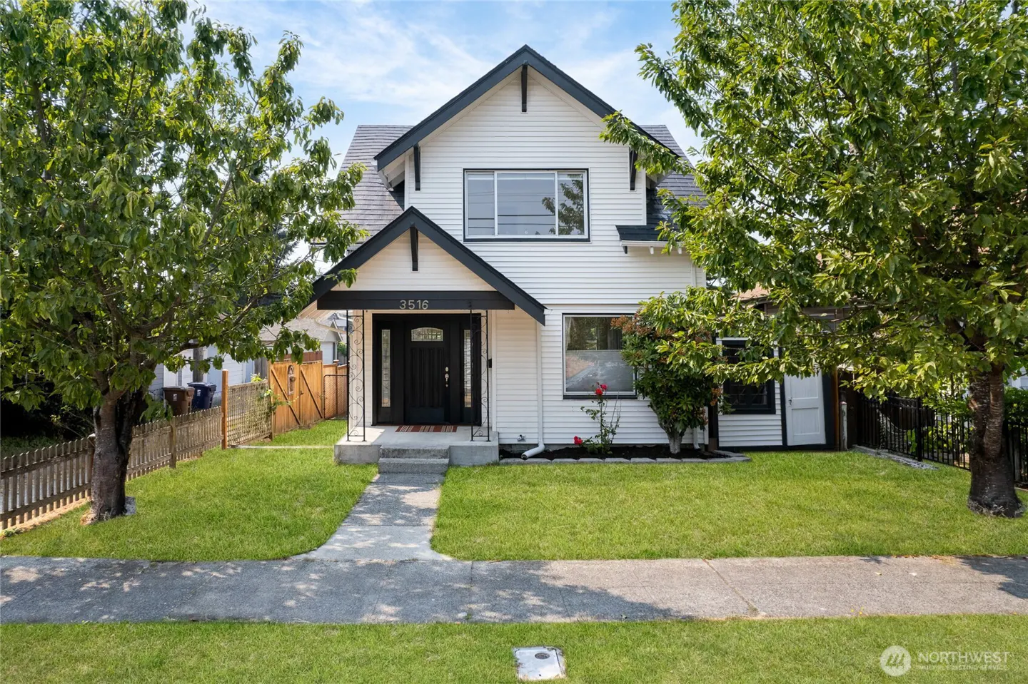 Two-story white house with black trim, a black front door, and a green lawn. Trees frame the house.