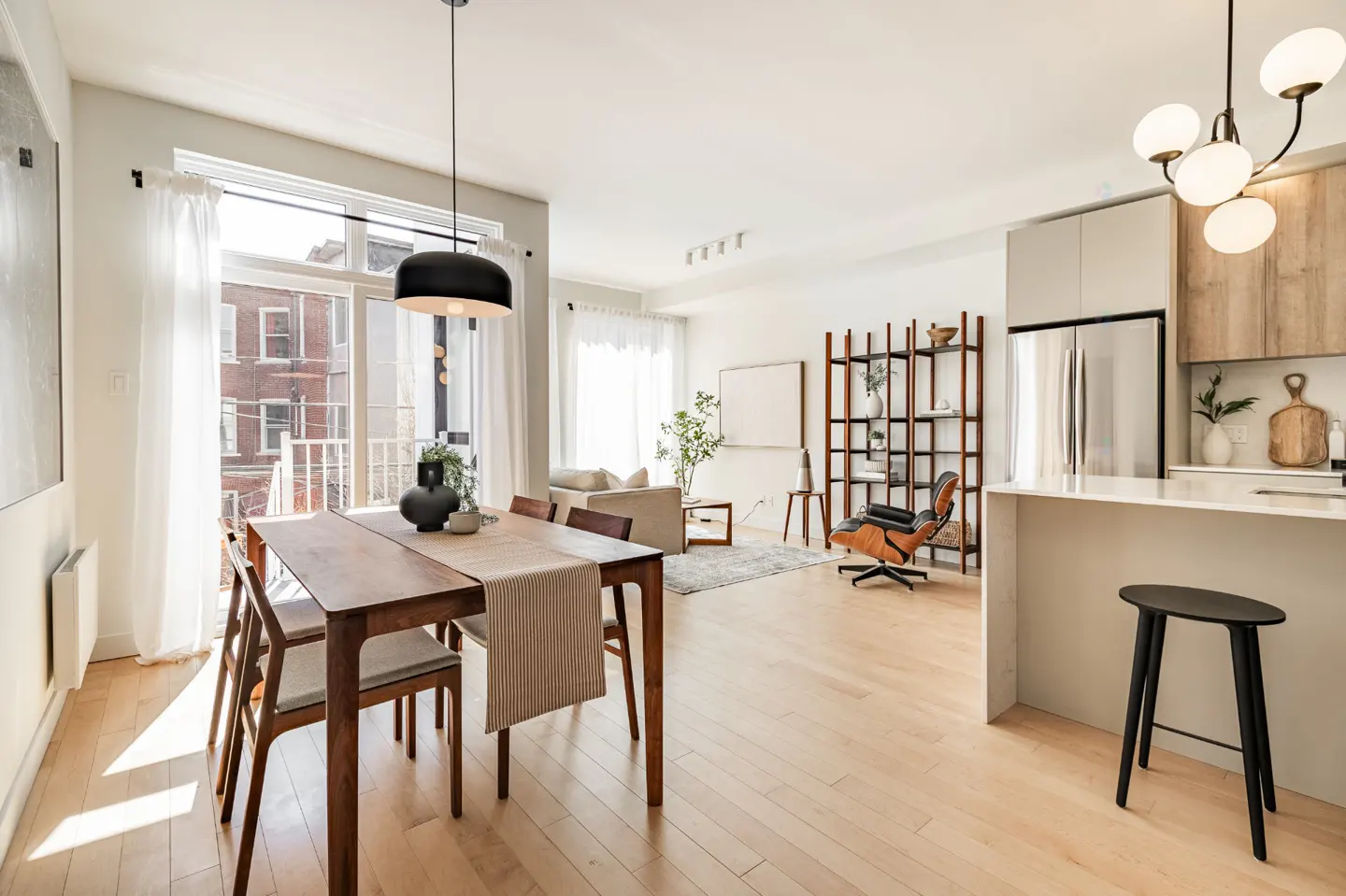 Bright, open-concept apartment with wood floors. Dining table with chairs, living area with sofa, and kitchen with island and stool.