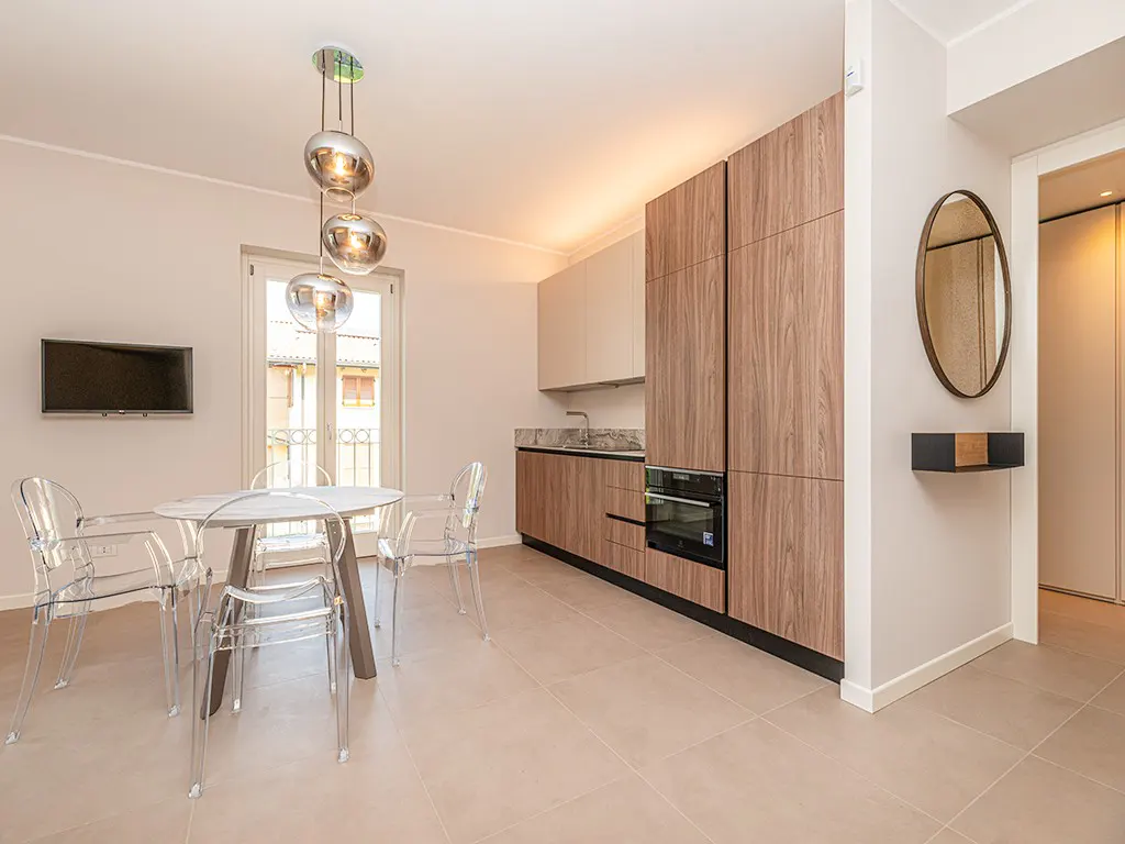 Modern kitchen with wood-grain cabinets, a round table with clear chairs, pendant lights, and a wall-mounted mirror.
