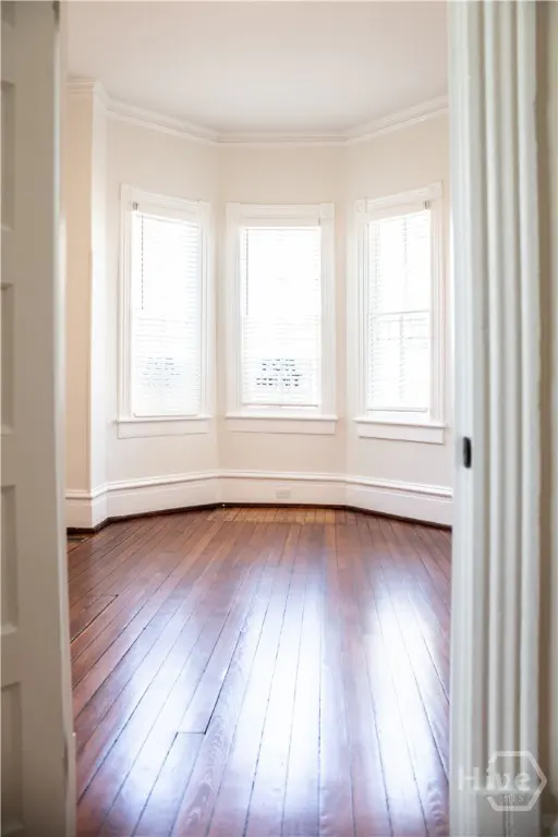Empty room with hardwood floors, white walls, and three windows with blinds. A white door frame is on the right.