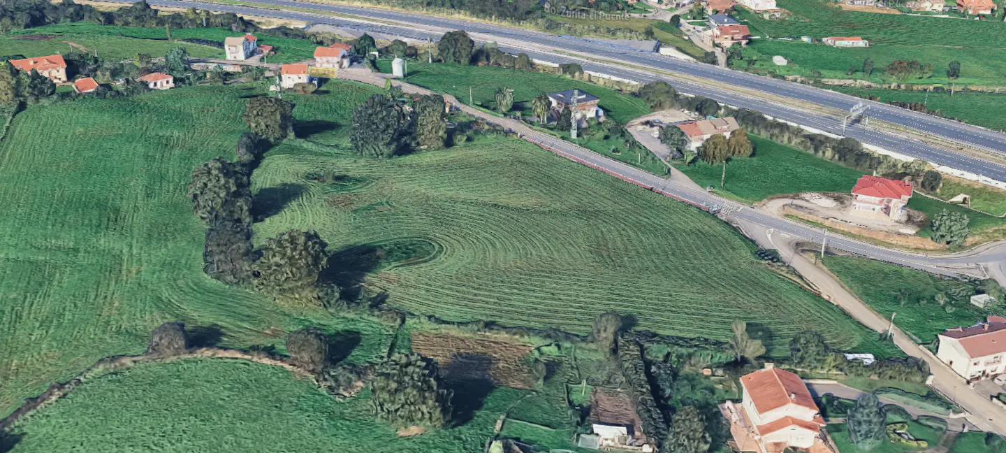 Aerial view of a large green field with houses, trees, and a highway in the background.
